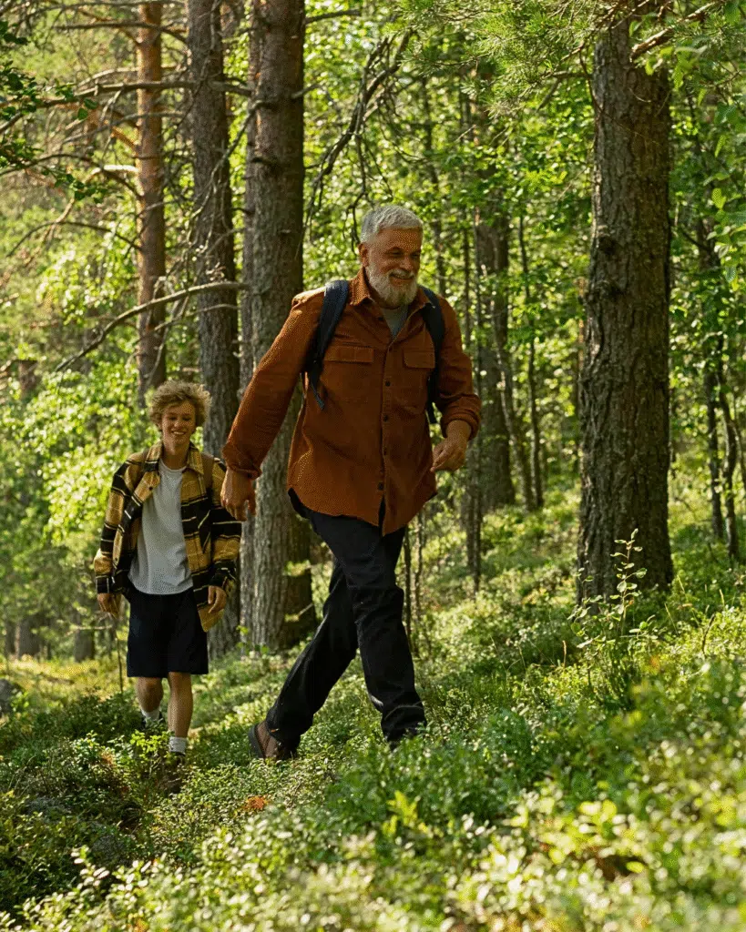 Older man and young boy hiking together through a sunlit forest.
